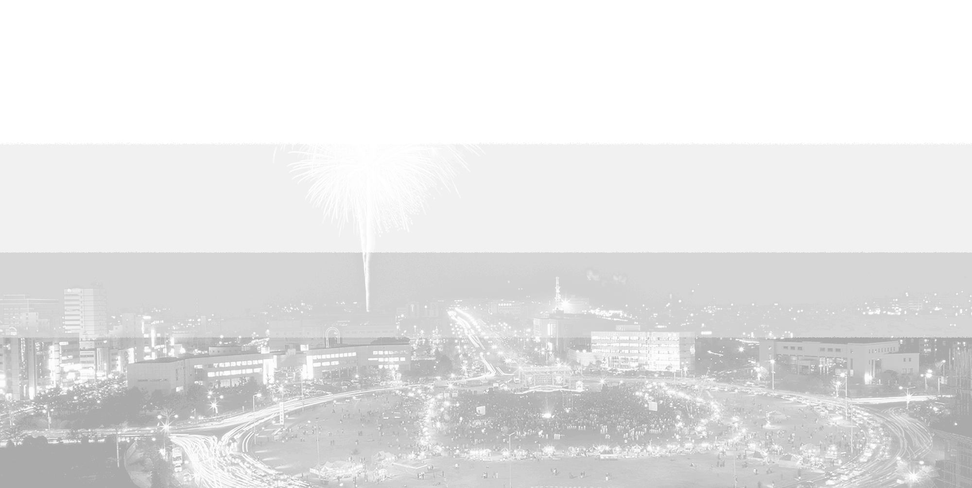 Black and white aerial night cityscape with fireworks bursting over a plaza filled with crowds, illuminated streets