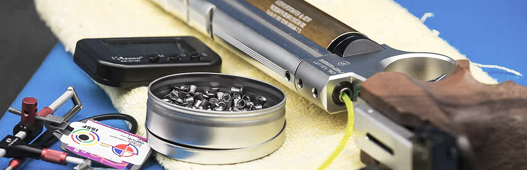 Close-up still life of a pistol with a tin of pellets and small tools on a cloth in metallic and blue tones